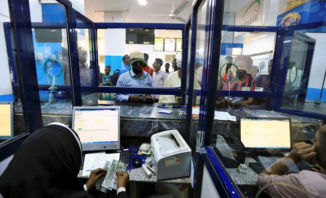 A cashier counts US Dollars as people wait to receive money inside Bab Al-Mandab Exchange transfer money bureau in Khartoum, Sudan on October 7, 2017. (Reuters)