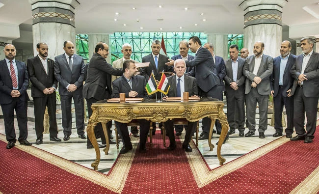 Hamas's new deputy leader Salah al-Aruri (seated L) and Fatah's Azzam al-Ahmad (seated R) sign a reconciliation deal in Cairo on Thursday, October 12, 2017, as the two rival Palestinian movements ended their decade-long split following negotiations overseen by Egypt. (AFP / KHALED DESOUKI)