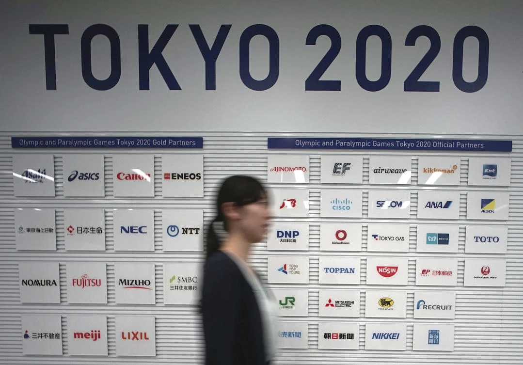A staff walks by a board featuring logos of Tokyo 2020 Summer Olympics sponsor companies in Tokyo. (AP)