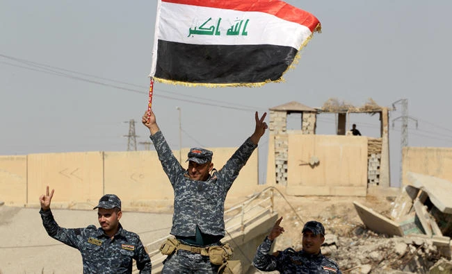 Iraqi forces pose with a natinoal flag as they stand on a river bank across Kurdish peshmerga positions on October 14, 2017, on the southern outskirts of Kirkuk. (AFP)