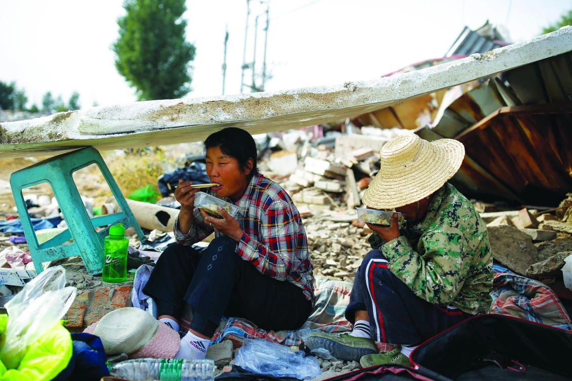 Migrant workers Wang Qin (left) and her sister Wang Jun eat lunch during a break from collecting scrap materials from the debris of demolished buildings on the outskirts of Beijing. (Reuters)