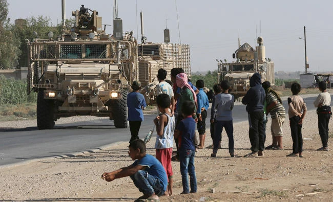 In this July 26, 2017 file photo, Syrian children and youths gather on a street as they look at a U.S. armored vehicle convoy pass on a road that links to Raqqa, northeast Syria. (AP)