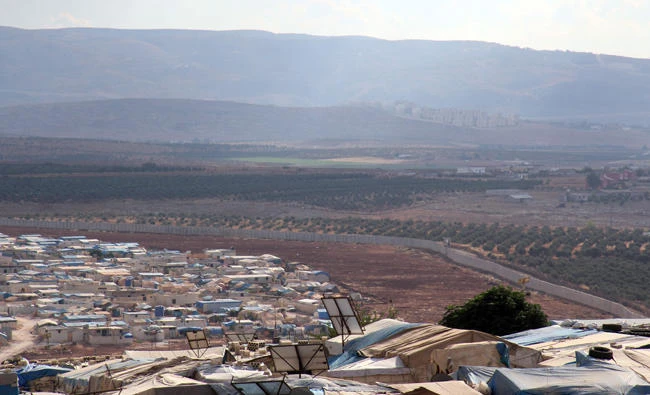 A picture taken on October 11, 2017, from the Syrian village of Atme in the northwestern province of Idlib shows a refugee camp (bottom) next to a three-metre high fortification, built by the Turkish government along its border with Syria. (AFP)