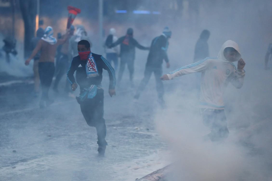 Football fans run from tear gas as they clash with police a few hours prior to kick off of the French L1 football match between Marseille (OM) and Paris Saint-Germain (PSG) on Sunday in Marseille. (AFP / Valery Hache)