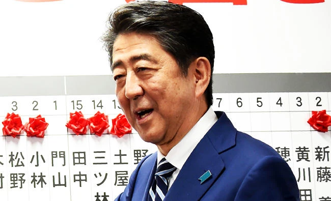 Japan's Prime Minister and ruling Liberal Democratic Party leader Shinzo Abe smiles as he puts rosettes by successful general election candidates' names on a board at the party headquarters in Tokyo on Sunday. (AFP)