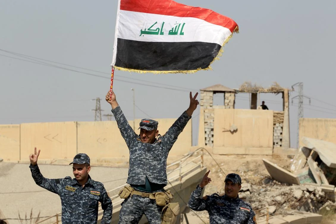 File: Iraqi forces pose with a natinoal flag as they stand on a river bank across from Kurdish peshmerga positions on the southern outskirts of Kirkuk.