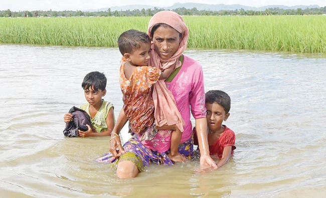 Rohingya refugee Khalida, a mother of three children, wades across a canal near the no man’s land area between Bangladesh and Myanmar. (File: AFP)