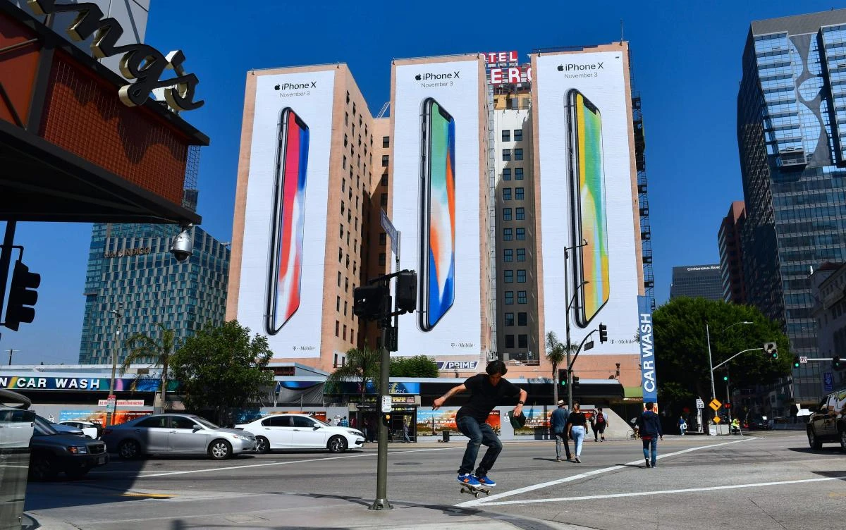 A skateboarder jumps the curb crossing a street in Los Angeles, California on October 13, 2017, where advertising for Apple's new iPhone X, due for release on November 3, covers the sides of three highrise buildings. (AFP)