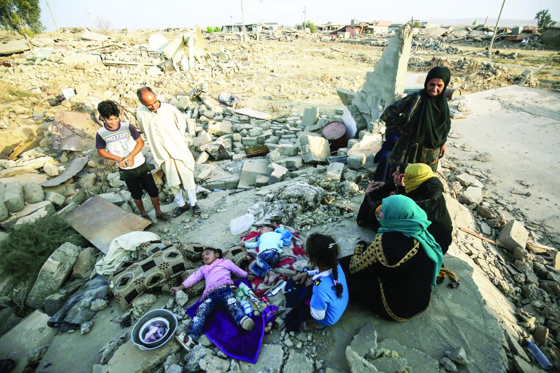 An Iraqi family sits on the rubble of their home in the village of Barzan in the Zummar area of Nineveh province, northwest of Mosul, on Friday. (AFP)