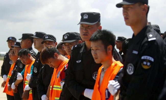 Chinese nationals, in orange vests, who were arrested over a suspected internet scam are escorted by Chinese police officers before they were deported at Phnom Penh International Airport. (Reuters)