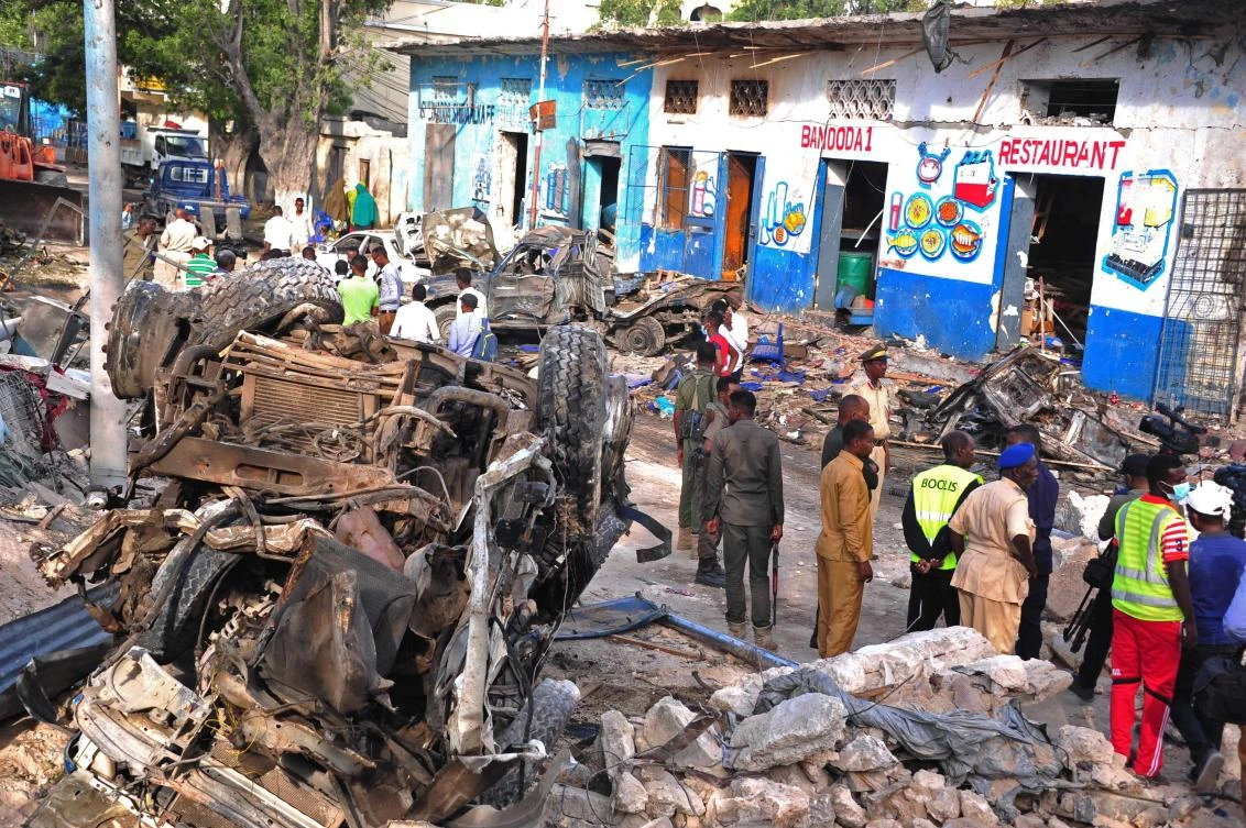 Somali security forces and civilians walk among damages at the scene of a blast on Sunday, a day after two car bombs exploded in Mogadishu. (AFP)