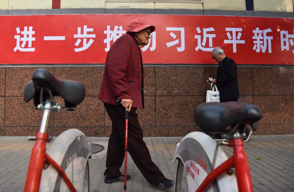 People walk past part of a slogan beside a road in Beijing. The Chinese characters read “Promote Xi’s thought of socialism with Chinese characteristics in the new era, making it a lively practice in Beijing.” (AFP/Greg Baker)