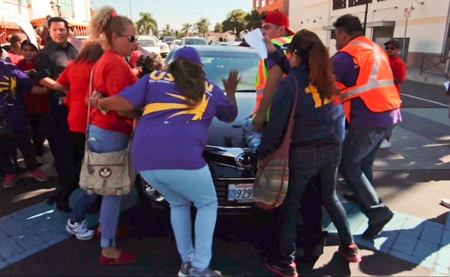 In this still image taken from video and released by Unite Here Local 11, demonstrators try to stop a motorist from driving his car into an immigrant rights rally in Brea, California, on Oct. 26, 2017. (Antonio Mendoza/Unite Here Local 11 via AP)