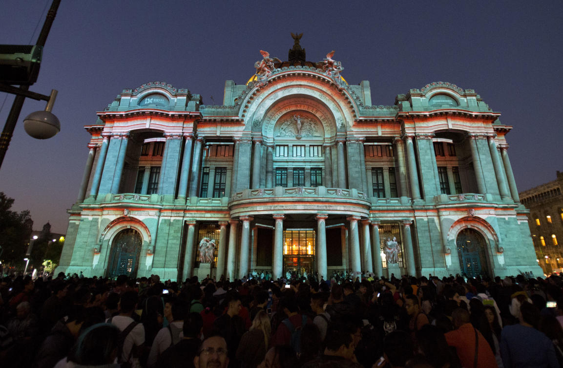 People gather to watch a light projection entitled "Nocheztli, the sacred color," by animation studio Kaijus Versus Robots, on the facade of the Palace of Fine Arts, during the International Festival of Lights in Mexico City, Friday, Nov. 17, 2017. This year's festival, featuring installations and projections, is lighting up the capital's historic center until Nov. 19.(AP Photo/Rebecca Blackwell)