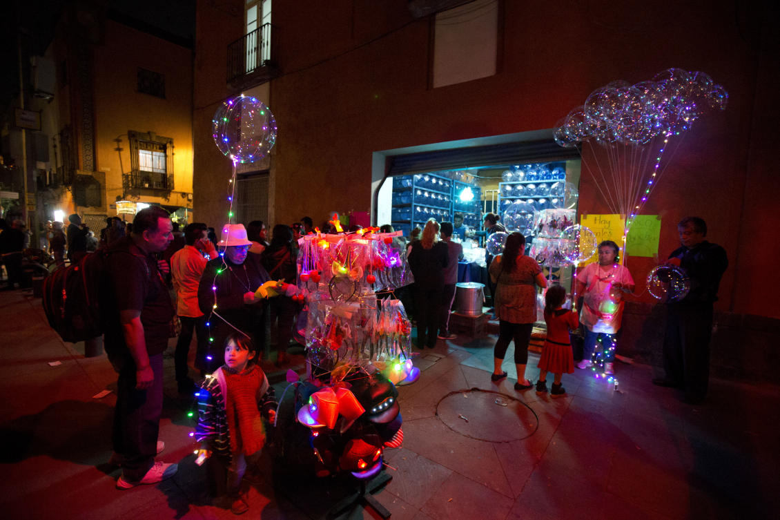 A little girl holds a balloon with lights inside as street vendors sell lit toys and souvenirs during the International Festival of Lights in Mexico City, Friday, Nov. 17, 2017. This years festival, featuring installations and projections, is lighting up the capital's historic center until Nov. 19. (AP Photo/Rebecca Blackwell)