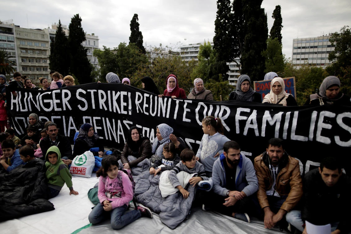 Refugees seeking reunification with family members in Germany sit in front of a banner announcing a hunger strike during a protest near the parliament building in Athens, Greece, Nov. 1, 2017. (Reuters/Alkis Konstantinidis)