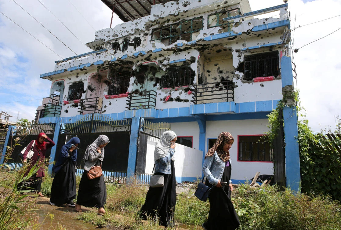 Residents who returned from evacuation centers walk past a bullet-ridden house believed to have been rented by pro-Daesh militant group leaders Isnilon Hapilon and Omar Maute before their attack on the region, in Basak, Malutlut district in Marawi city. (Reuters)