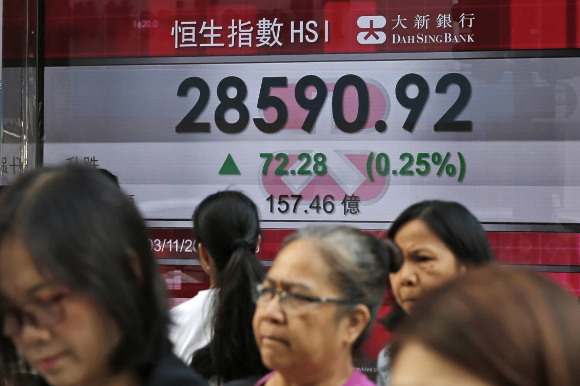People walk past an electronic stock board showing the Hang Seng Index at a bank in Hong Kong, Friday, Nov. 3, 2017. (AP/Kin Cheung)