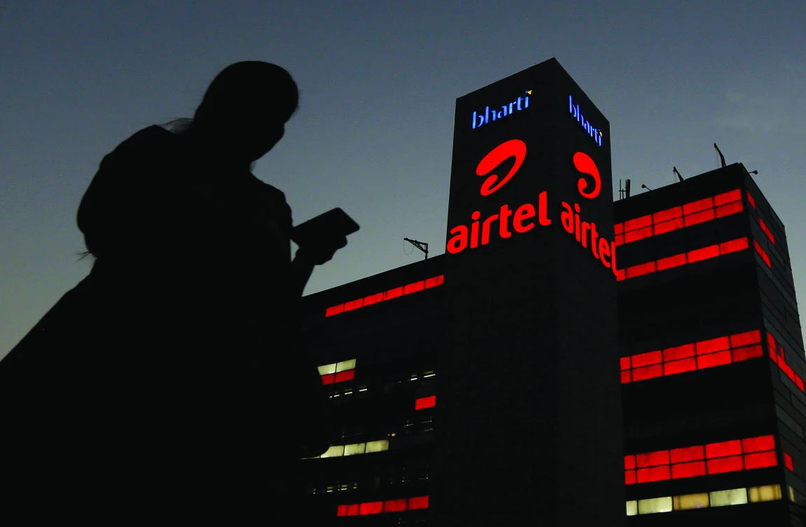 A girl checks her mobile phone as she walks past the Bharti Airtel office building in Gurugram. Qatar is offloading a $1.5 billion stake in the telecom company as it comes under pressure to raise funds at home. (Reuters)