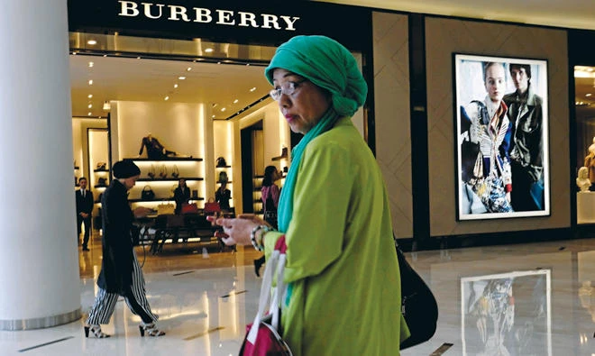 A woman stands in front of a Burberry shop at a shopping mall in Jakarta. Shares in the British fashion icon plunged Thursday after it said sales will stagnate for the next two years. (Reuters)
