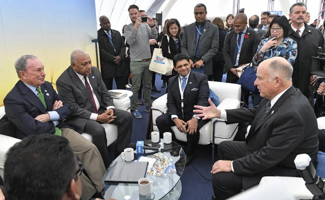 Former New York Mayor and billionaire Michael Bloomberg, left, speaks with Fiji prime minister and COP president Frank Bainimarama, beside him, and California Governor Jerry Brown, right, in the US Climate Action Center at the COP 23 Fiji UN Climate Change Conference in Bonn, Germany, on Saturday, Nov. 11, 2017. (AP Photo/Martin Meissner)