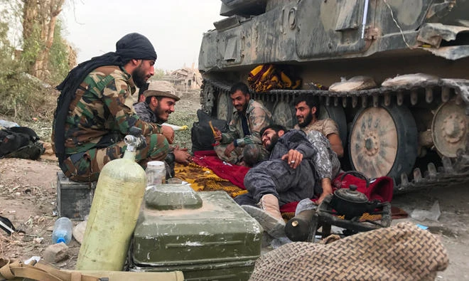 Syrian government forces sit next to an armoured vehicle in a northeastern district of Deir Ezzor on November 5, 2017, after retaking the city from Daesh group jihadists. (AFP)