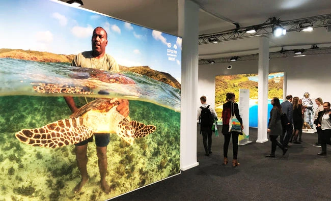 Delegates walk past a poster showing a man holding a turtle and other photos from the Pacific Islands during the COP23 UN Climate Change Conference 2017, hosted by Fiji but held in Bonn, Germany, in this November 10, 2017 photo. (REUTERS)