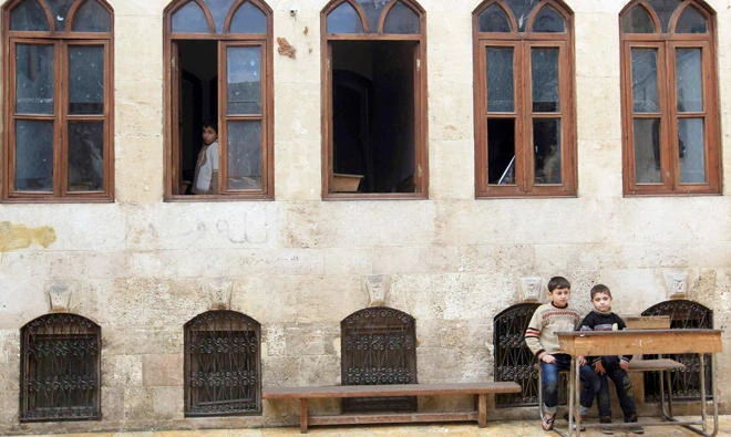 File: Two boys sit at a desk as another stands at a window inside a school in Old Aleppo. (Reuters)