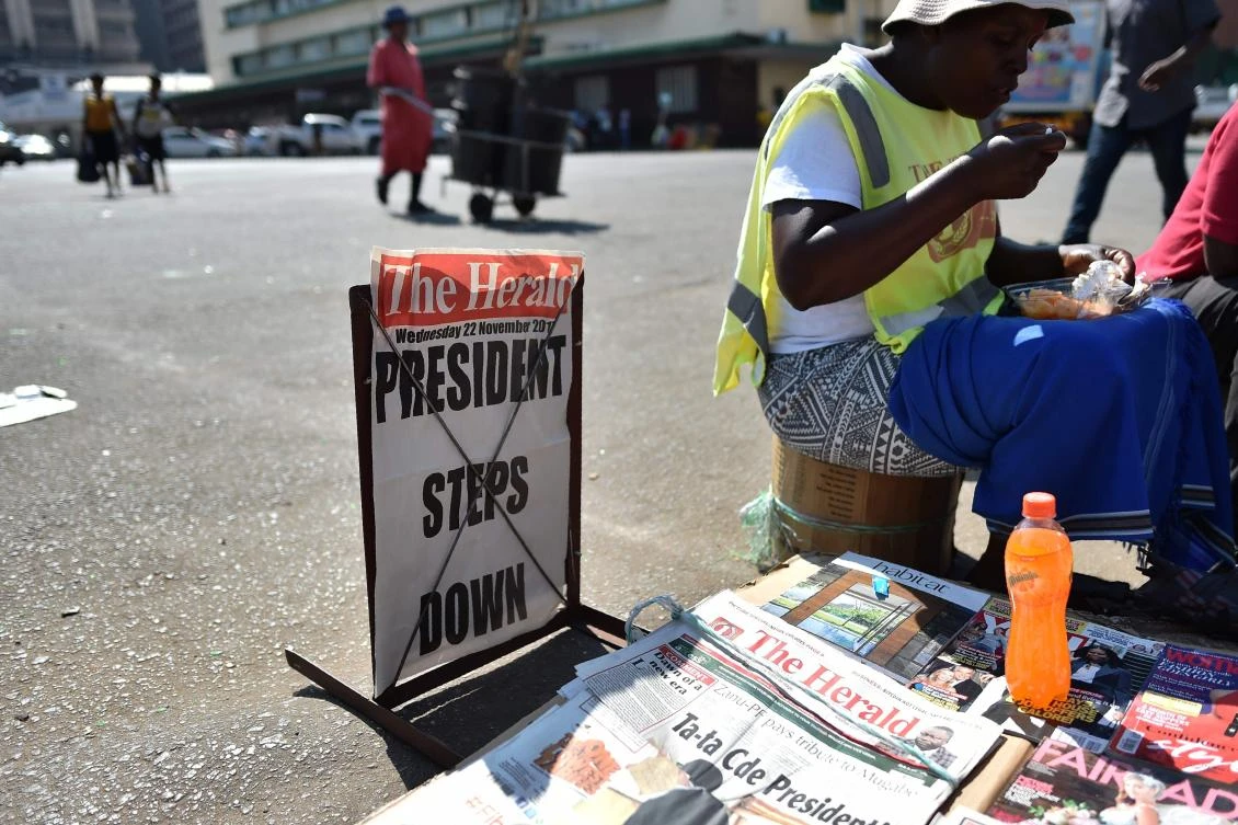 Above, a man holds a newspaper stand on a street corner in Harare on November 22. Zimbabweans woke up to the first day in 37 years without Mugabe in power. (AFP)