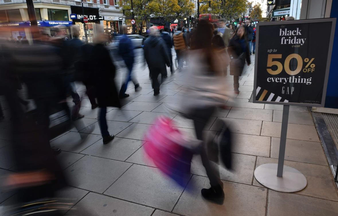 Shoppers pass a promotional sign for 'Black Friday' sales discounts as they exit a retail store on Oxford Street in London. (AFP)