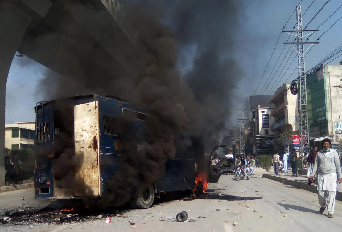 Pakistani residents walk past a burning prison van torched by protesters during clashes with police in Rawalpindi on November 25. (AFP)