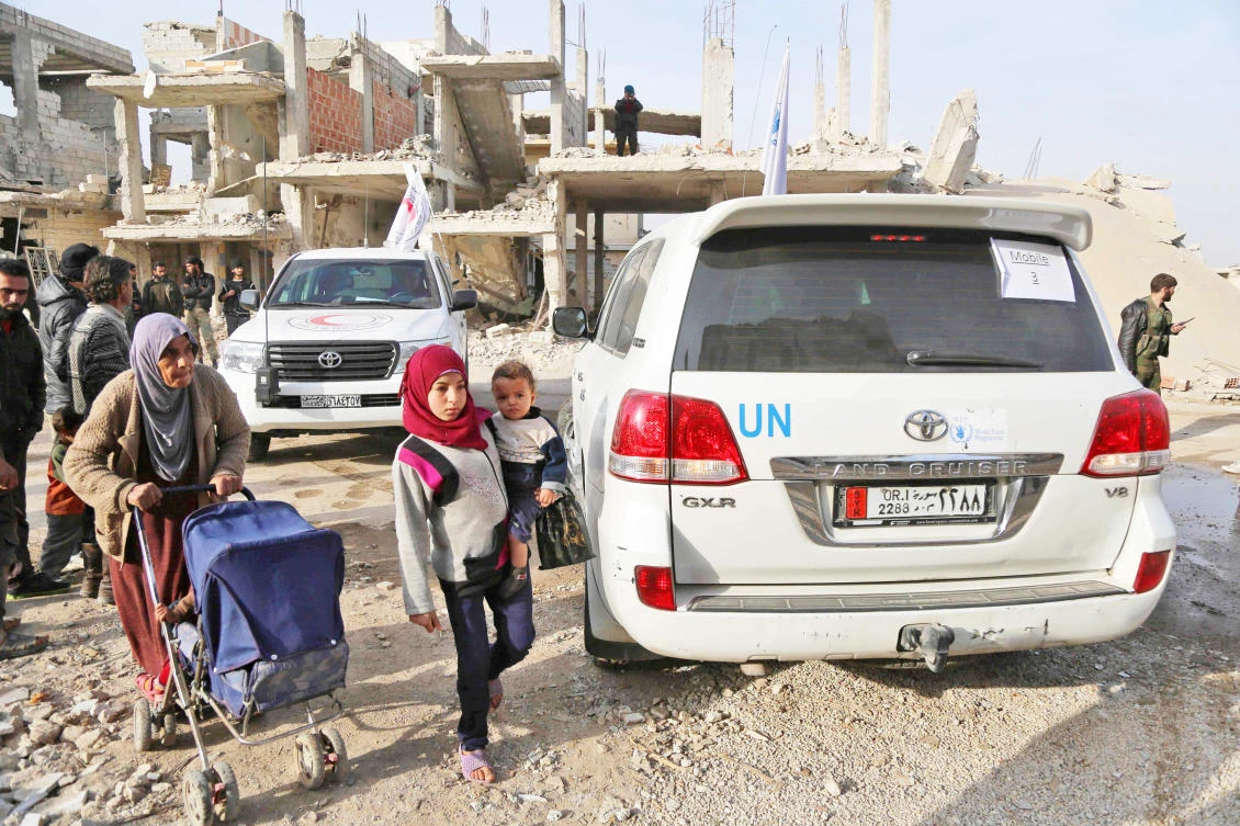 Syrians walk past vehicles of the International Committee of the Red Cross (ICRC) and the UN during a humanitarian delivery in the Nashabiyeh town, Eastern Ghouta, on Tuesday. (AFP)
