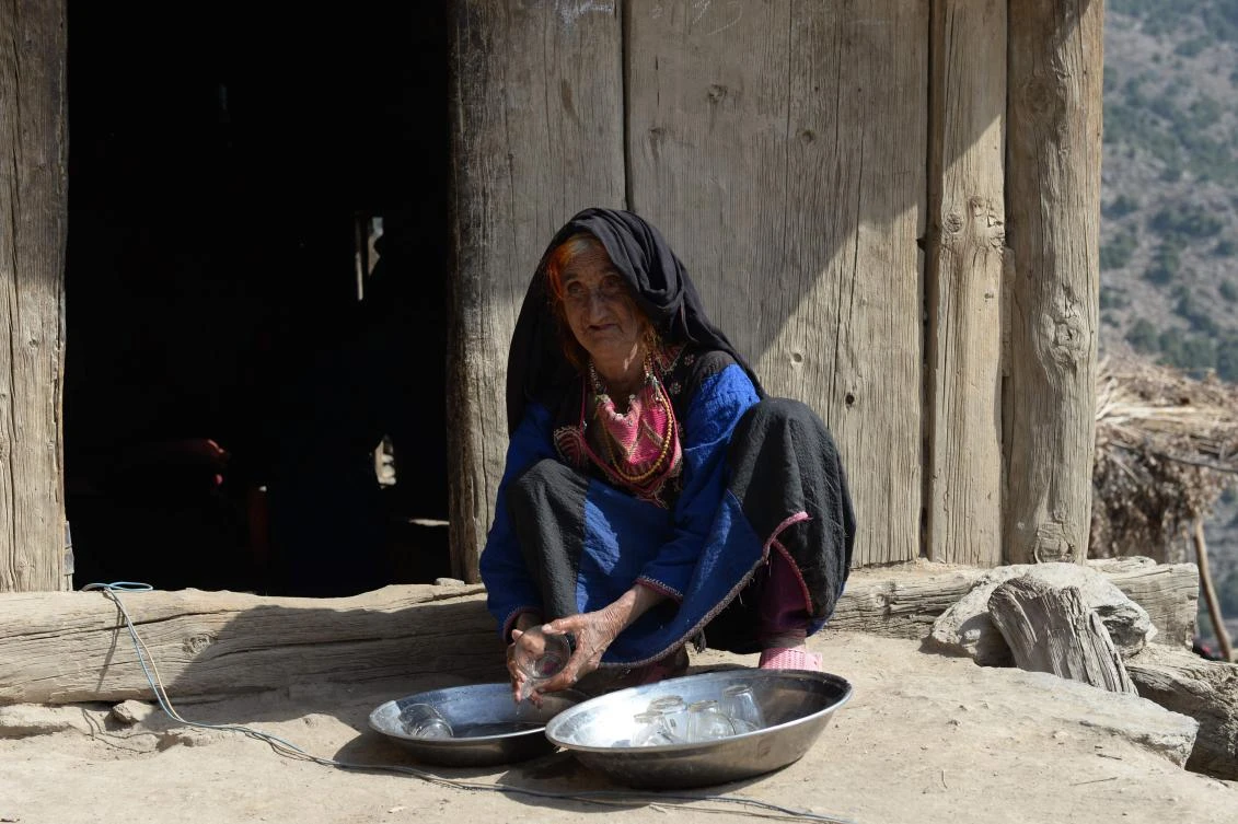 In this photograph taken on October 25, 2017 Afghan widow Janat Bibi, 65, washes a glass outside her mud house in the remote village of Shemol in the eastern province of Nangarhar. (AFP)