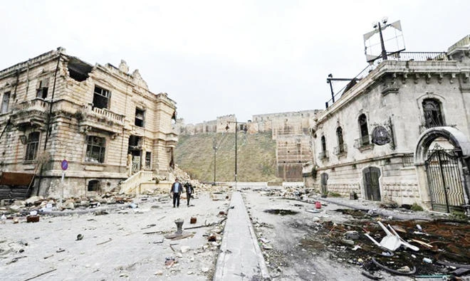 People walk past the old customs buildings, left, and Peoria restaurant, right, near Aleppo's historic citadel, in the regime-controlled area of the city, last year. (File photo/Reuters)