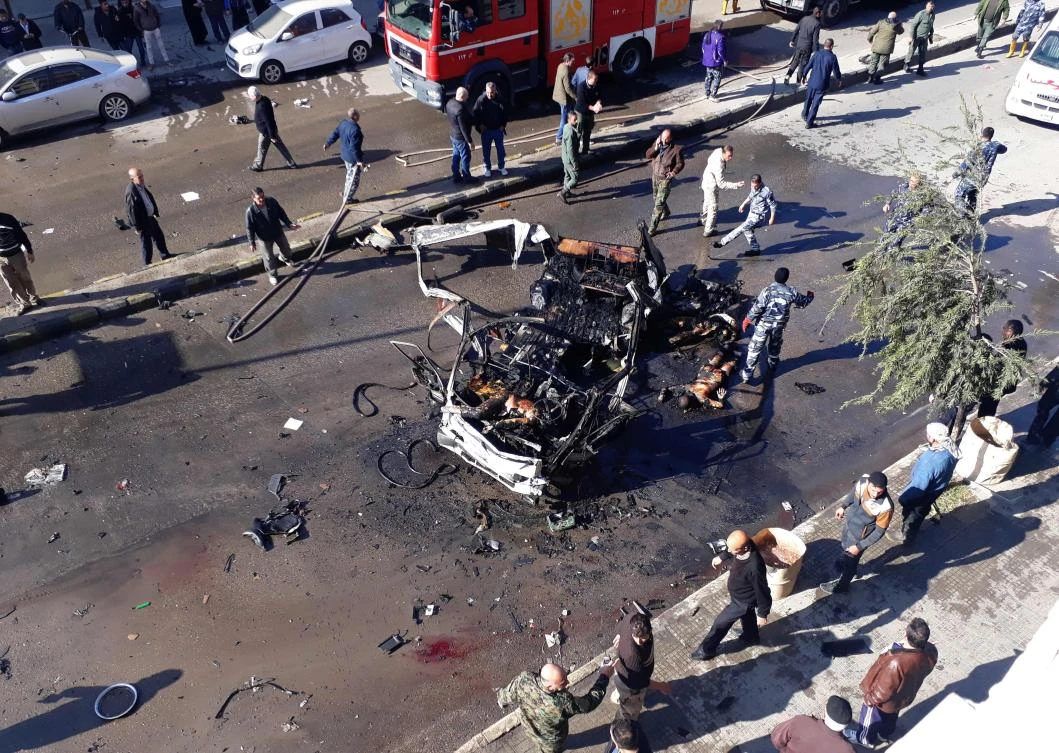 Civilians watch on as members of the Syrian Arab Red Crescent collect the bodies of victims of a car bomb explosion in a predominantly pro-government neighborhood of the central Syrian city of Homs on Dec. 5, 2107. The blast rocked a street in a neigborhood mostly inhabited by members of the Alawite minority to which President Bashar Assad belongs, the Syrian Observatory for Human Rights said. (AFP)