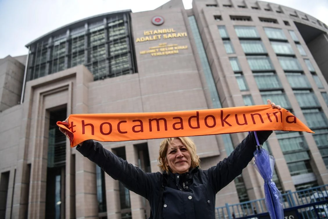 Protesters hold scarfes reading ” Do not touch my University- Do not touch my Academics” on December 5, 2017 in front of Istanbul’s courthouse, during a demonstration in support of a group of academics charged with terror offenses for signing a petition almost two years ago calling for peace in the Kurdish-dominated southeast. Over 1,120 Turkish and also foreign academics initially signed the petition which denounced the actions of Turkey’s military in the southeast where deadly clashes had erupted with outlawed Kurdish militants in 2015. The first 10 academics charged — from Istanbul University and Galatasaray University — went on trial on Dec. 5, 2017. (AFP/OzanKose)