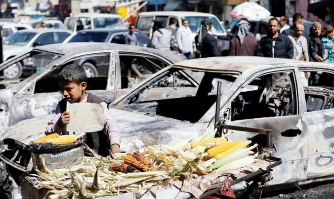 A boy sells on Tuesday grilled corn near cars damaged during clashes between the Houthis and forces loyal to Yemen’s former President Ali Abdullah Saleh in Sanaa. (Reuters)
