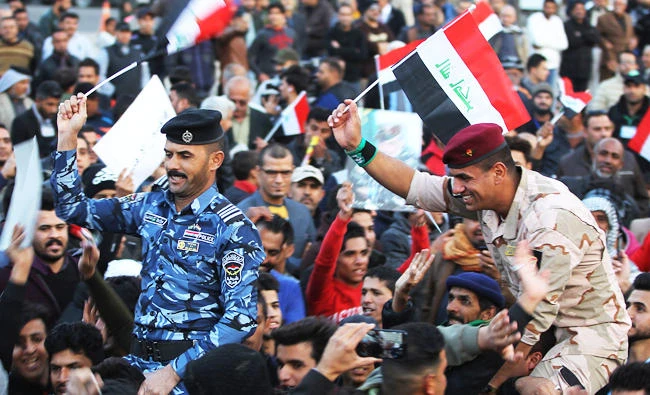 An Iraqi soldier and policeman wave their national flag in Baghdad's Tahrir Square on Sunday, during a gathering celebrating the end of the three-year war against the Daesh group. (AFP)