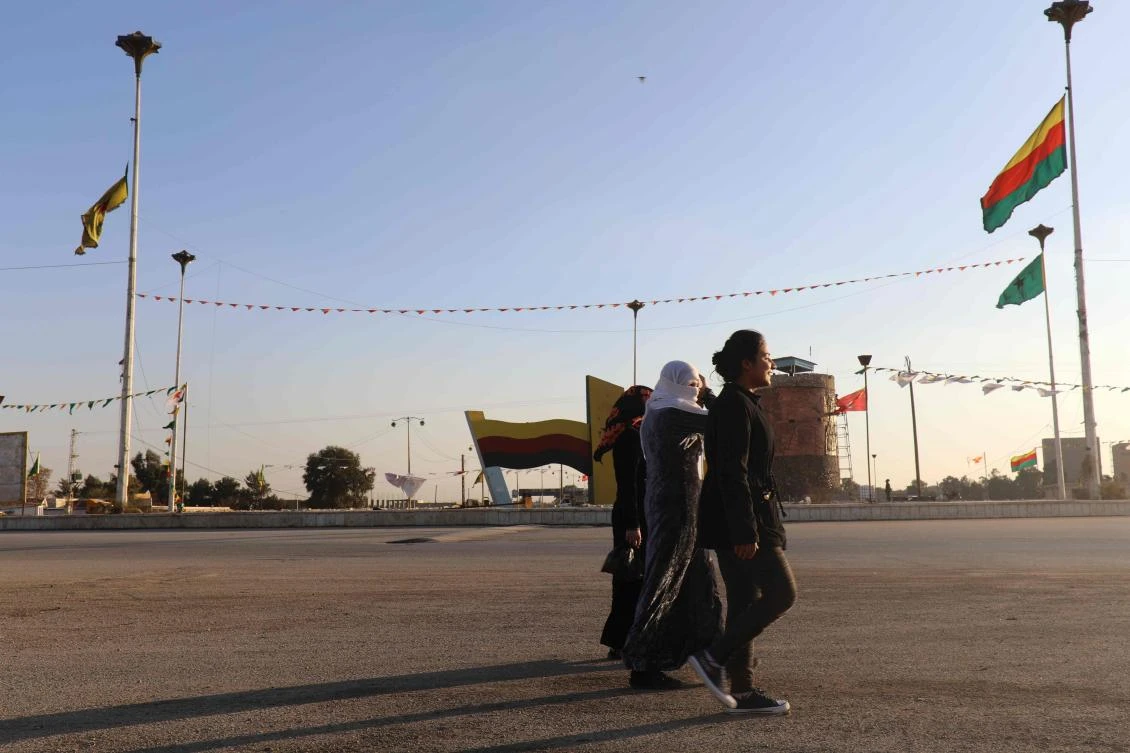 Syrian women walk in a street next to Kurdish flags in the northeastern city of Qamishli, on Nov. 30, 2017. (AFP)