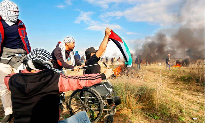 Wheelchair-bound Palestinian demonstrator Ibrahim Abu Thurayeh waves a Palestinian flag during a protest along the Gaza-Israel border on Dec. 15. (AFP)