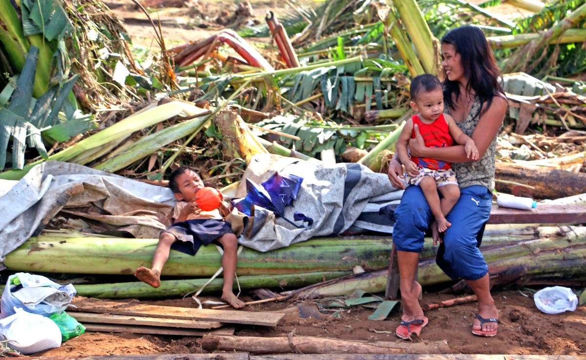 A mother sits with her children on fallen banana trees in Barangay San Mateo Borongan in Eastern Samar, Dec.17, 2017. (AFP)