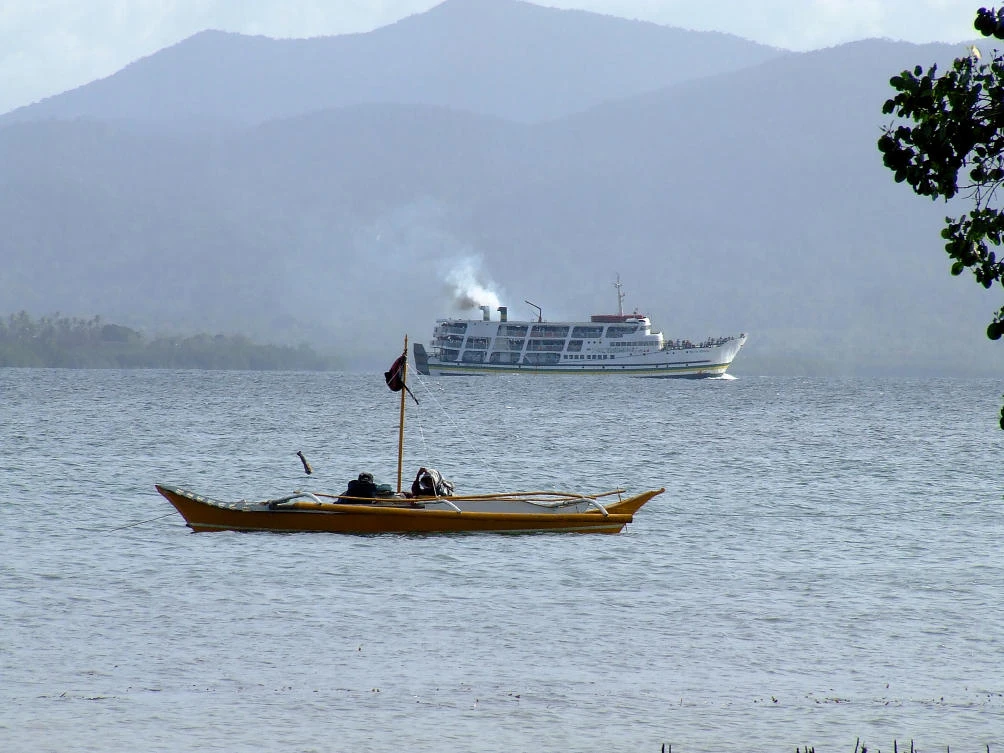 A small traditional fishing boat and a large passenger ferry. Philippines. (Shutterstock)