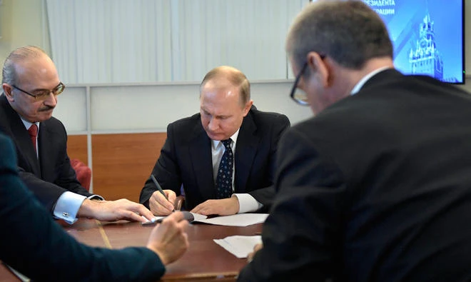 Russian President Vladimir Putin, center, signs a receipt while submitting his endorsement papers at the Central Election Commission in Moscow, Russia on Dec. 27, 2017. (AP)