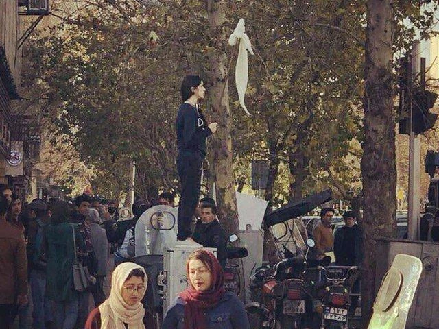 A woman in Iran protests in public without a headscarf, holding her compulsory hijab up on a stick. (Photo courtesy: social media)