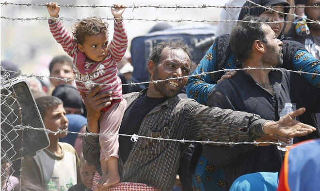 In this file photo, a Syrian refugee holds onto his daughter as he waits to cross into Turkey at Akcakale border gate in Sanliurfa province. (Reuters)