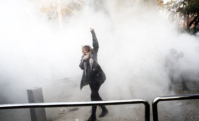 An Iranian woman raises her fist amid the smoke of tear gas at the University of Tehran during a protest driven by anger over economic problems, in the capital Tehran on Saturday. (AFP)