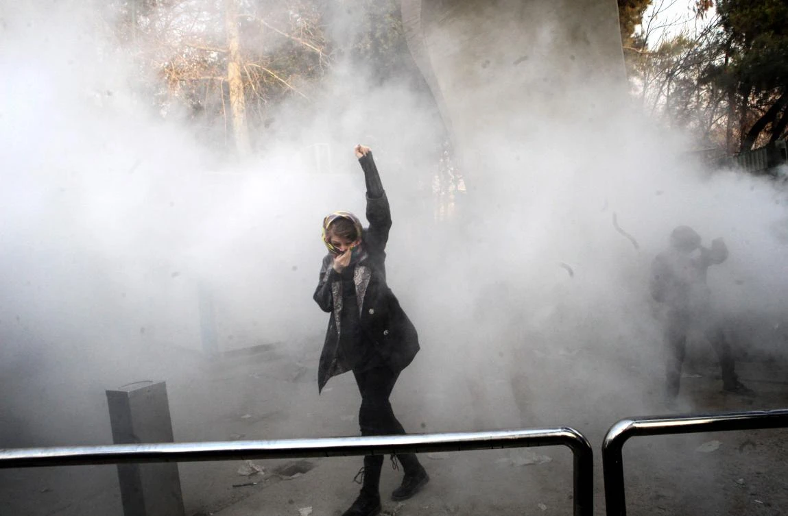 An Iranian woman raises her fist amid the smoke of tear gas at the University of Tehran during a protest driven by anger over economic problems. Students protested in a third day of demonstrations sparked by anger over Iran’s economic problems. (AFP)