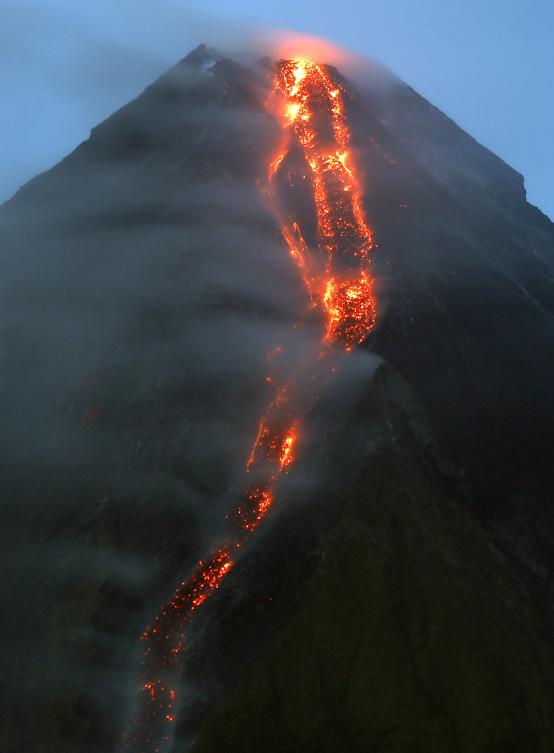 epa06445978 Red glowing lava flows down a slope of Mayon Volcano as seen from Legaspi city, Albay Province, Philippines, 17 January 2018. The Philippine Institute of Volcanology and Seismology Agency (PHIVOLCS) maintained the alert level at 3 (critical) on a scale of 5, citing an imminent major volcanic eruption, although it could take days or even weeks to occur. A total of 15,410 people living within a 6-kilometer radius of the crater, which has been designated as a danger zone, have been evacuated and housed in temporary shelters, schools and sports centers in the region. The government of the Albay province declared a state of emergency on 16 January 2018. EPA/FRANCIS R. MALASIG