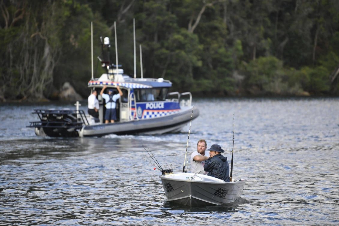 Fishermen guide their boat past a police vessel at the scene where a seaplane crashed into the Hawkesbury River, north of Sydney, Australia, Sunday, Dec. 31, 2017. The plane crashed into a river killing all six people on board, officials said. (Perry Duffin/AAP Image via AP)