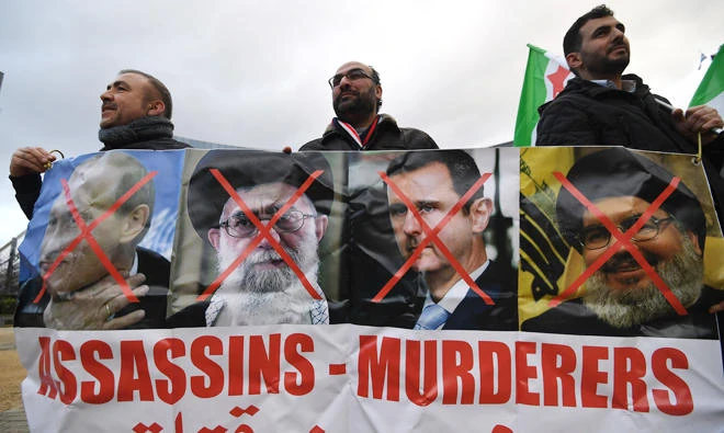 Protesters hold a banner with the crossed-out portraits of Russian President Vladimir Putin, Iranian Supreme Leader Ali Khamenei, Syrian President Bashar Assad and Hezbollah chief Hassan Nasrallah during a demonstration in support of the Iranian people in Brussels on Wednesday. (AFP)
